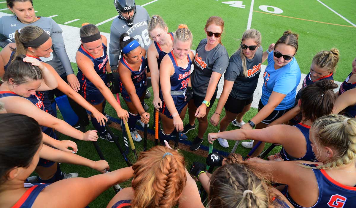 Field hockey team members putting their hands together in the middle of a circle