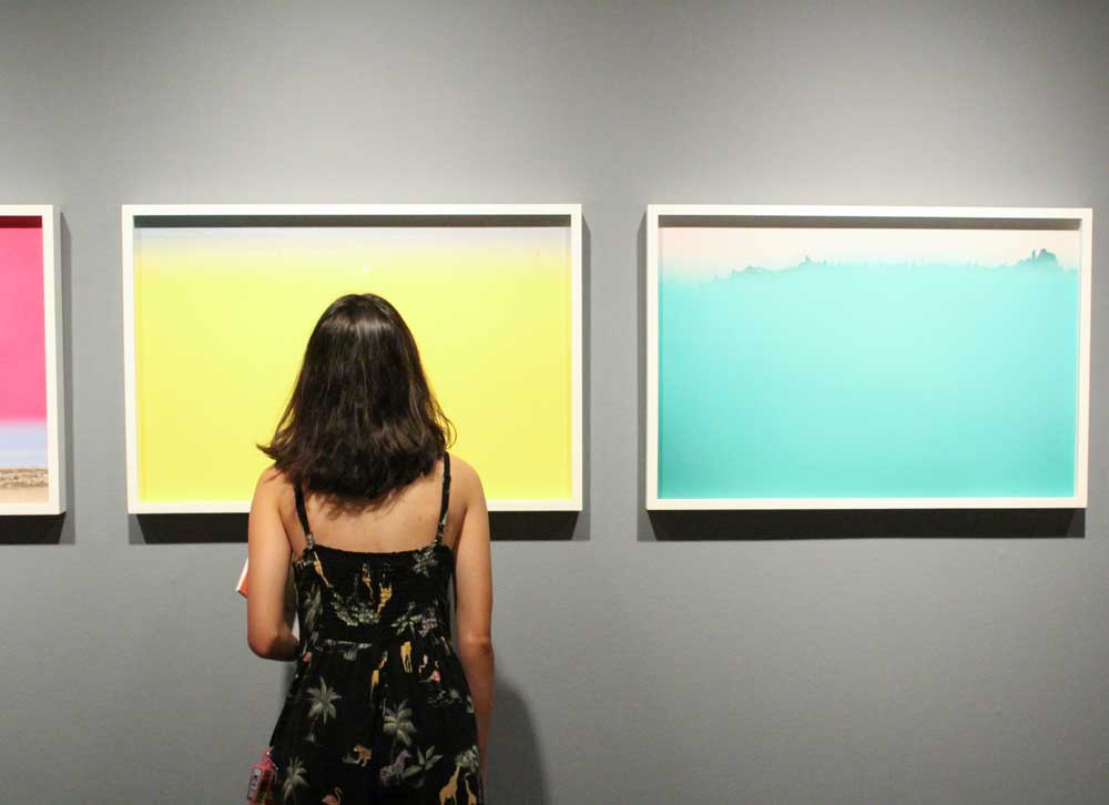 A woman standing in front of three colorful paintings