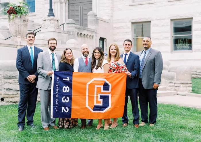 Gettysburg College alumni pose with a college banner outside a building.