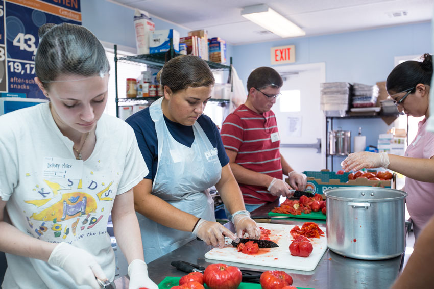 Students in campus kitchen cutting tomatoes