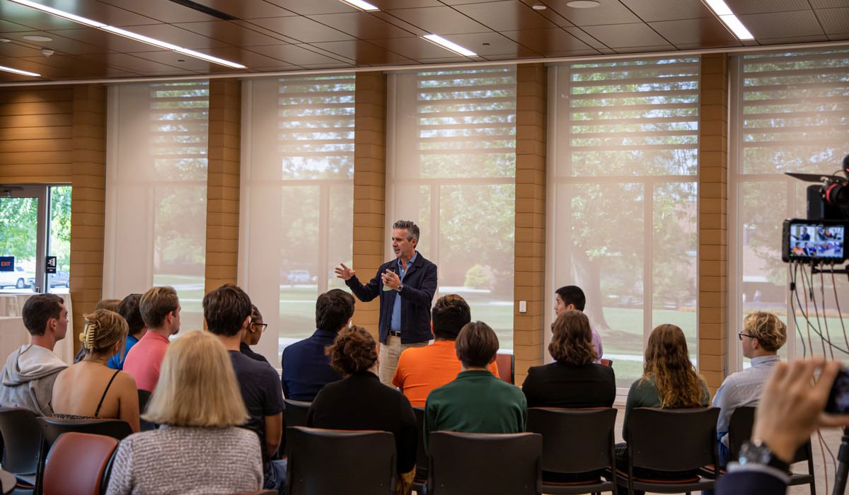 Photo of man holding microphone and speaking to crowd of students