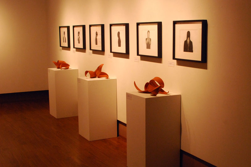 Clay sculptures on podiums with artwork on the wall behind them inside of an art gallery