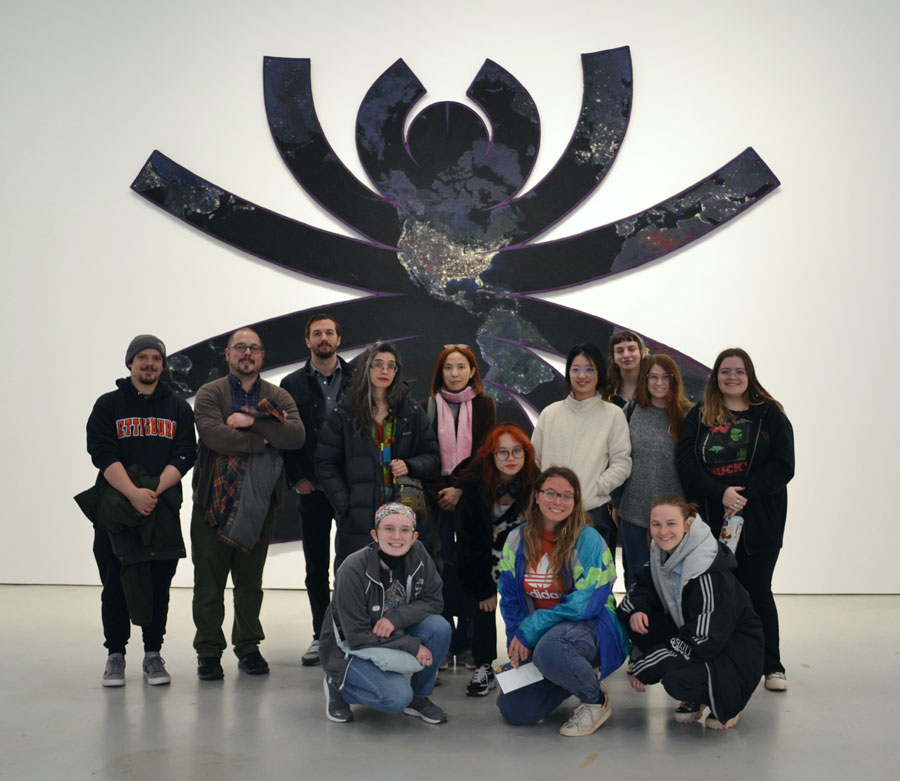 Artwork that resembles the shape of a spider with the continents superimposed on the surface of the artwork and students posing in front of it