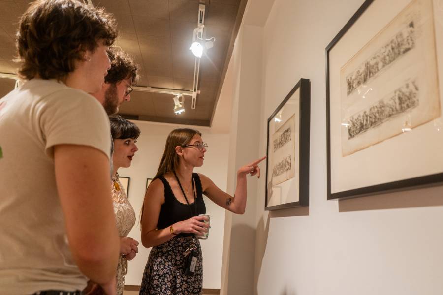 Gallery visitors examine framed prints as a guide points out details.