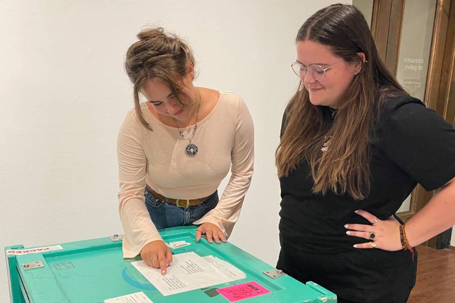 Students review paperwork on an art shipping crate.