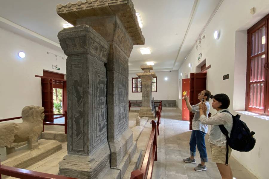 Visitors photograph carved stone pillars in a museum.