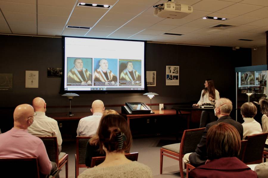 Student presents to an audience with portraits displayed on a screen.