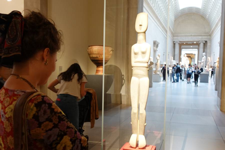 Visitor viewing a tall Cycladic-style marble figure in a museum gallery.