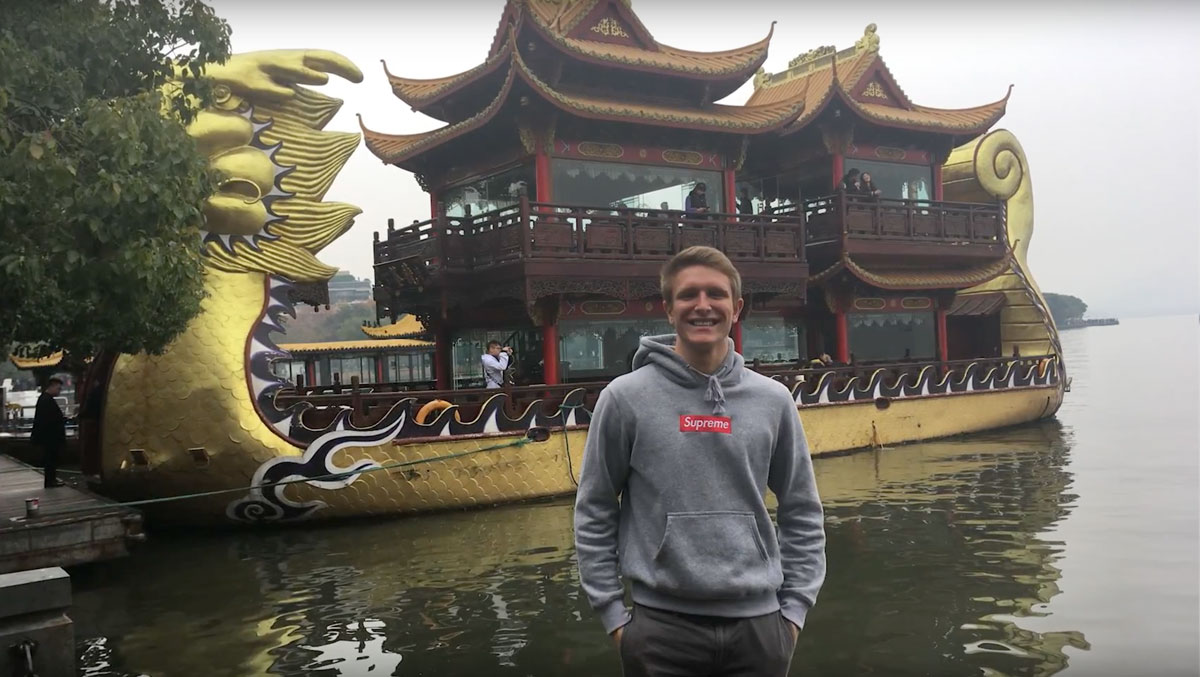 Tyler Mann 20 standing in front of a dragon boat in China
