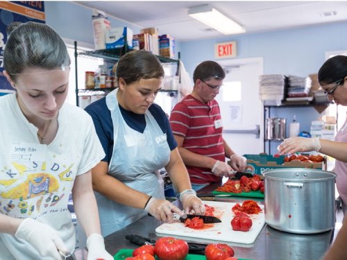 Students in campus kitchen cutting tomatoes
