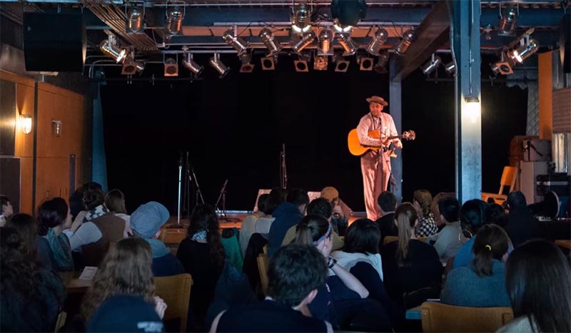 A performer standing on stage holding a guitar in front of audience members