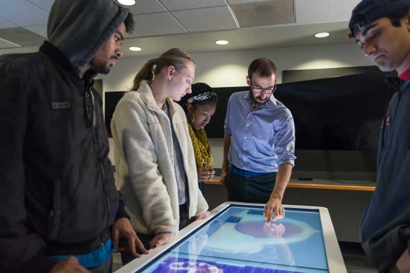 Faculty member giving a lecture to students in front of an anatomage table