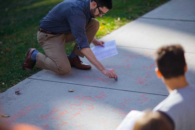 Faculty member and student drawing on a sidewalk with chalk