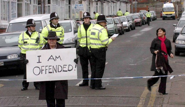 A man holding 'I am offended' sign with polices behind