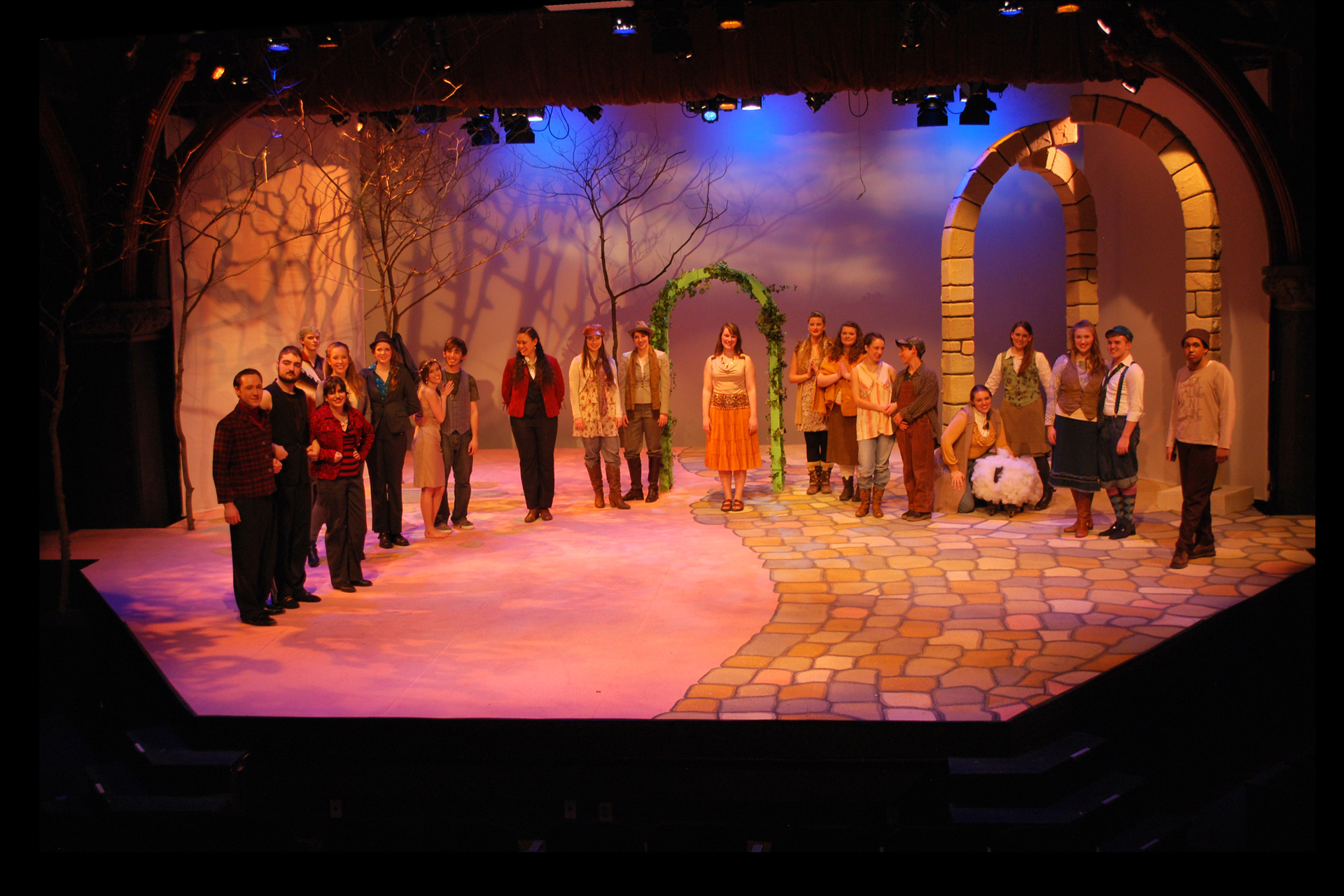 Actors and actresses in an outdoor stage setting with a stone archway