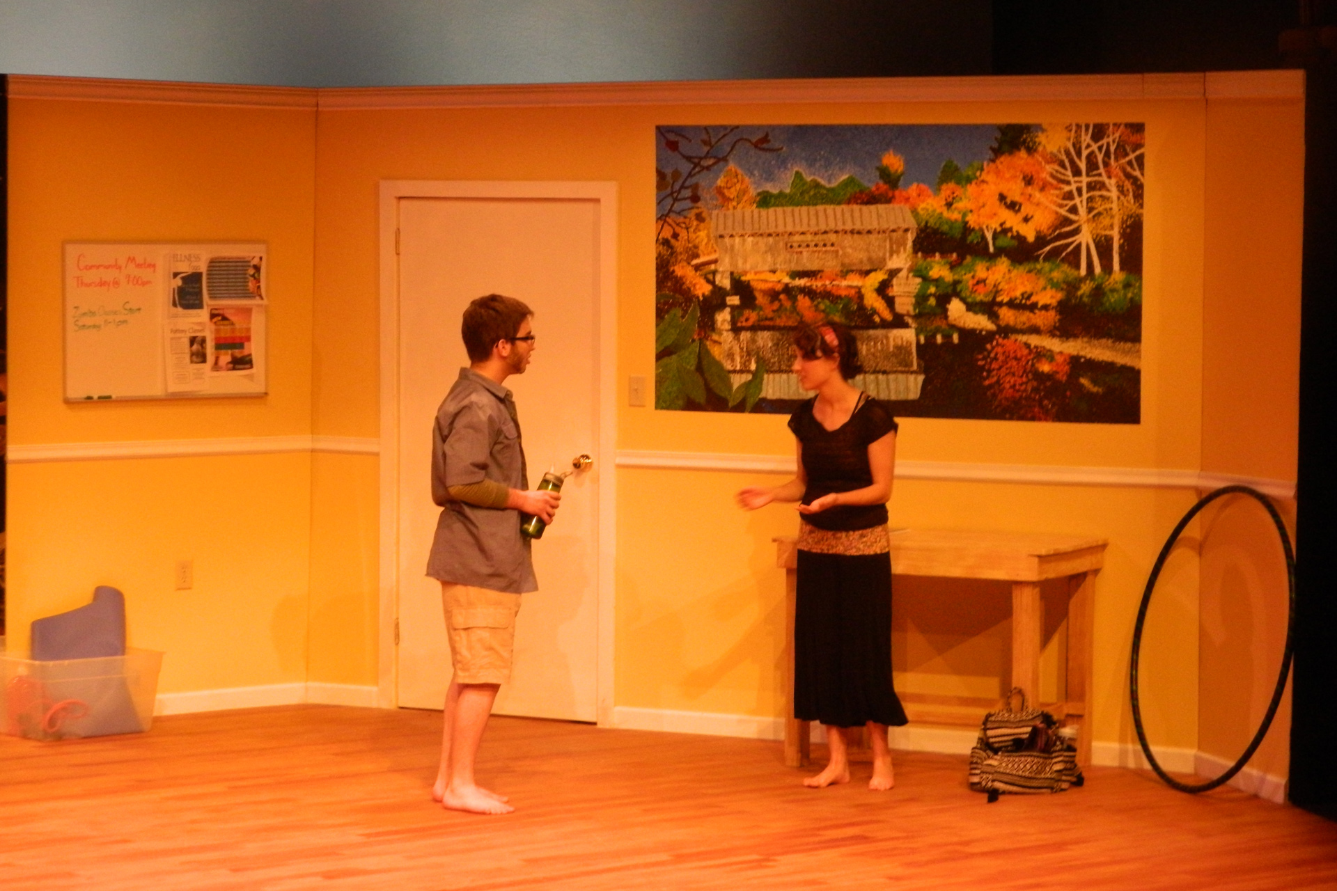 Actor and actress facing eachother in a yellow room with a painting on the wall
