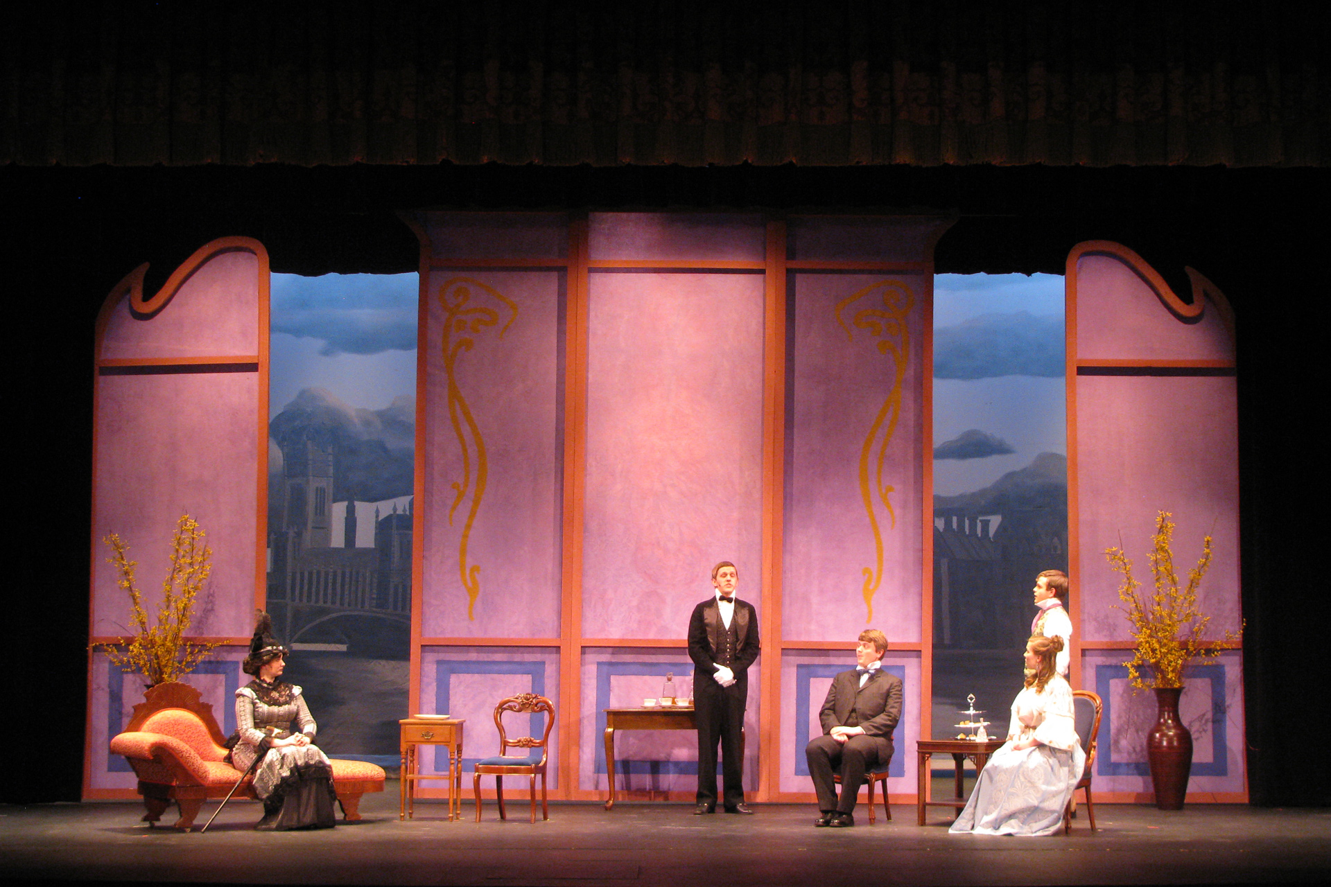 Man in tuxedo addresses a room of people in period attire