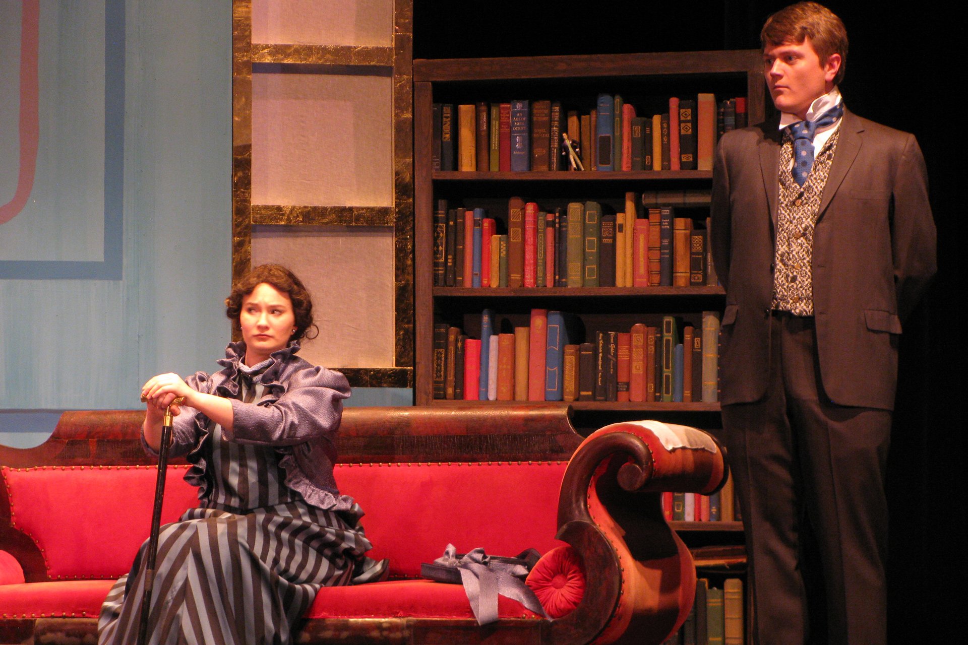 Woman in period attire sitting on a couch with a man on the left hand side