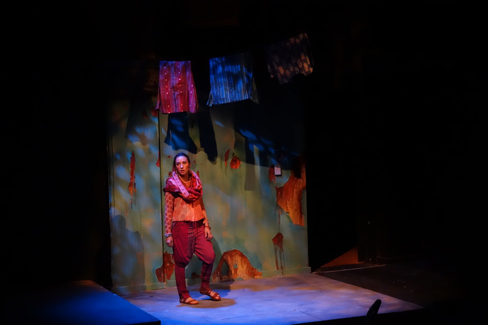 Woman standing on a dimly lit stage with clothes hanging above her