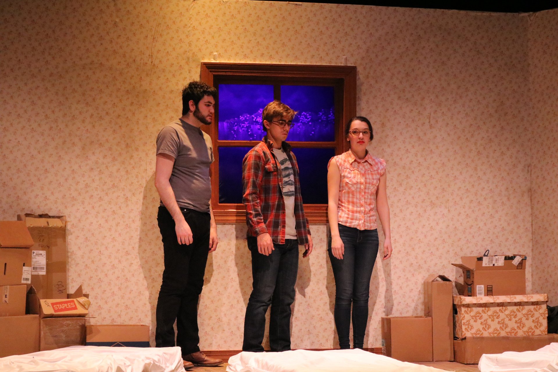 Three students standing in a room with boxes on the floor