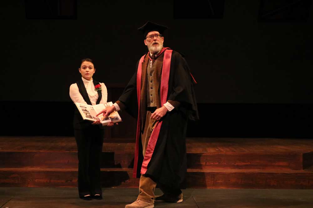 An older man in robes pointing at a book that is being held open by a younger woman
