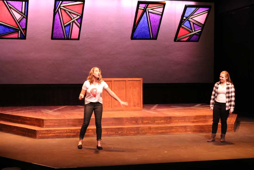 One woman on stage singing with another woman on stage to the right