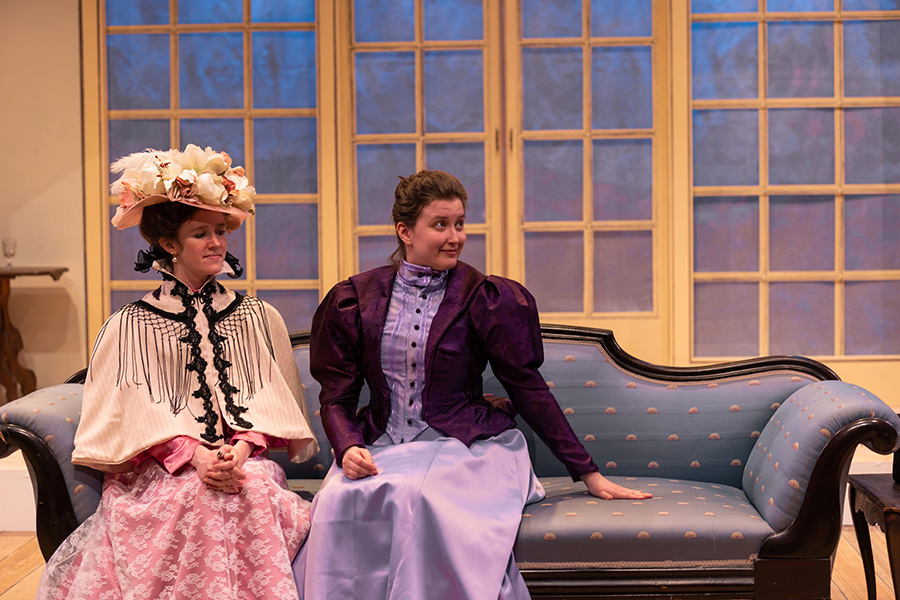 2 ladies sitting on a couch on stage.