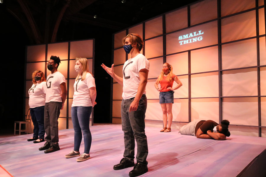 Students standing on stage wearing shirts with large letters on the chests