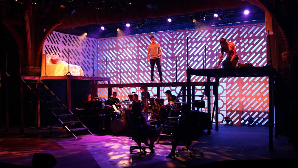 Actor standing on top of an elevated stage with musicians playing below