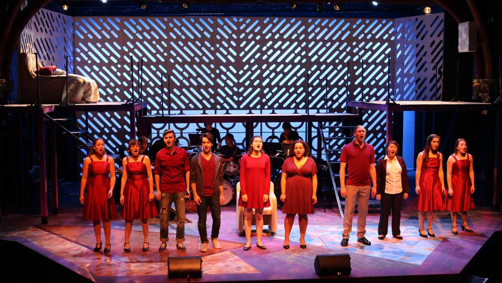 Multiple actors and actresses dressed in red performing on stage