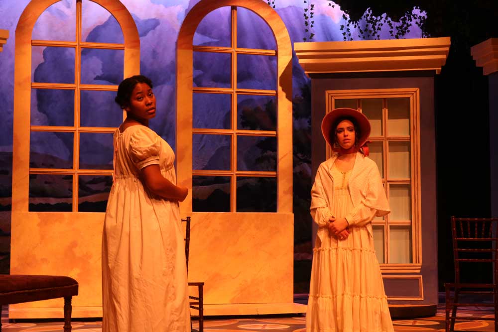 Two female actresses gazing towards the audience with Victorian windows behind them