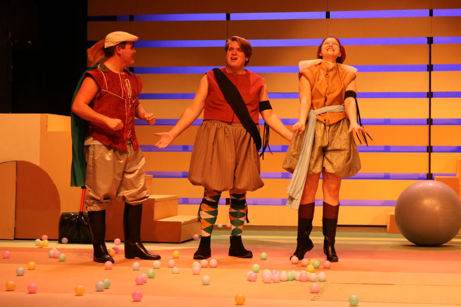 Two men and a woman standing side by side on stage making different faces and gestures