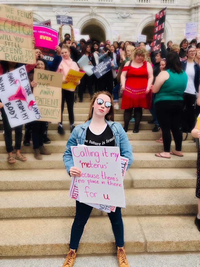 Grace Verbrugge standing at a protest with a sign