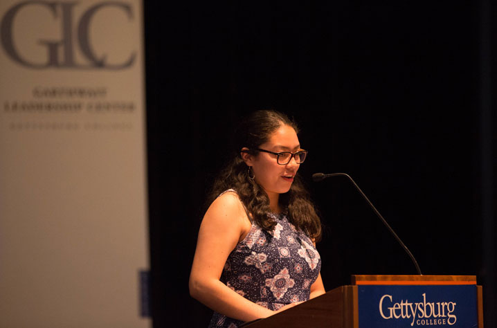 Student speaking at podium with GLC logo behind her