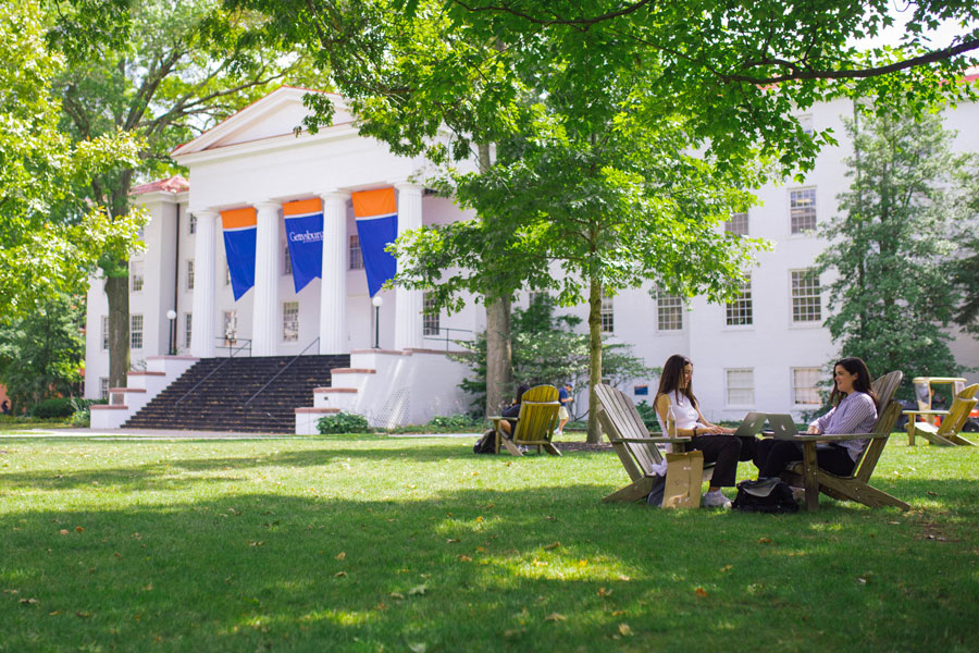 Two students sitting on their laptops in front of Penn Hall