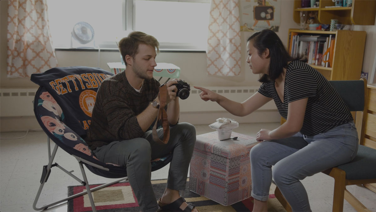 Two students sitting and investigating a camera in residence room