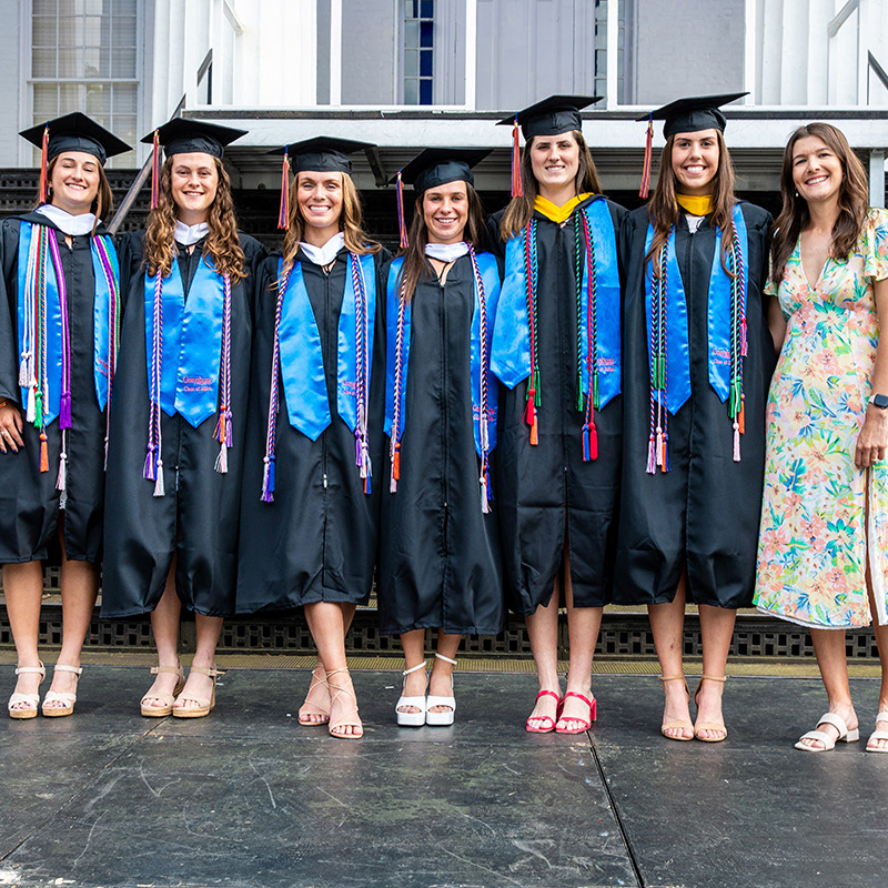 Six women’s lacrosse seniors and their Head Coach stand in front of Penn Hall