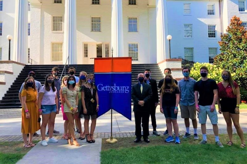 High school age students standing outside Penn Hall with a College banner