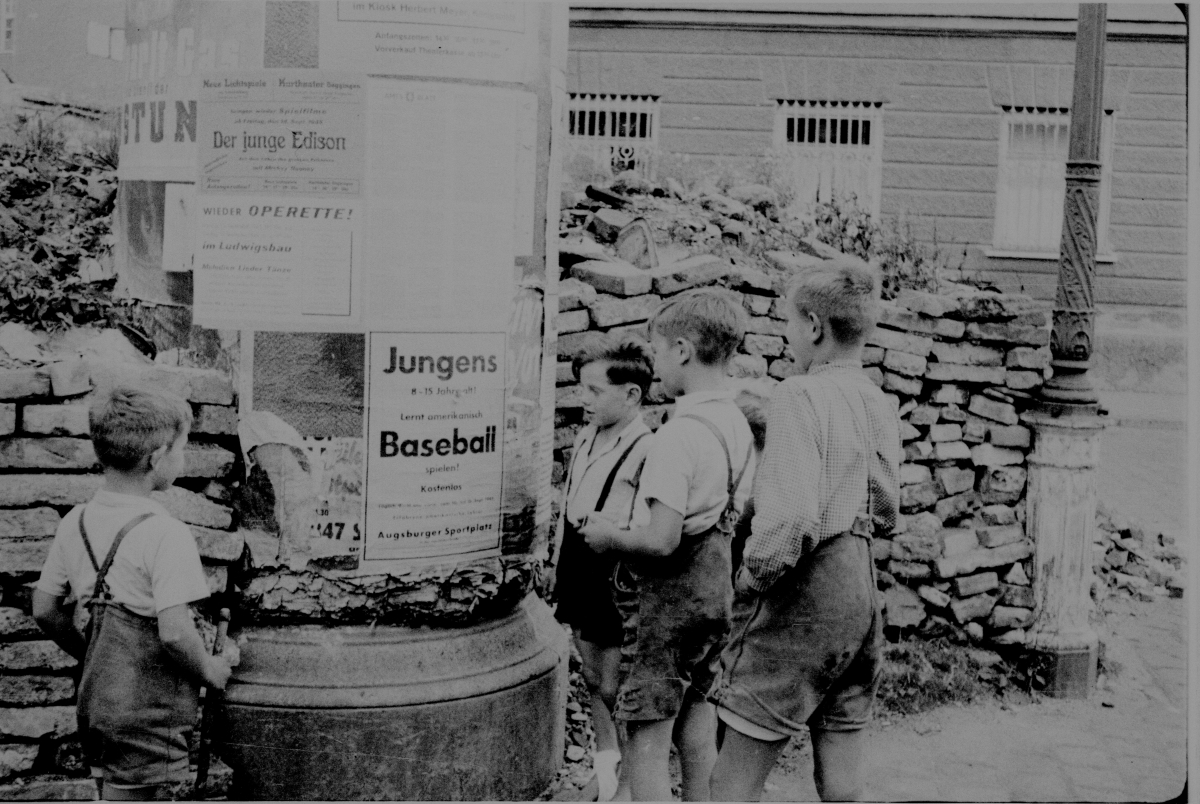 Four boys looking at baseball game posters standing next to a rock wall