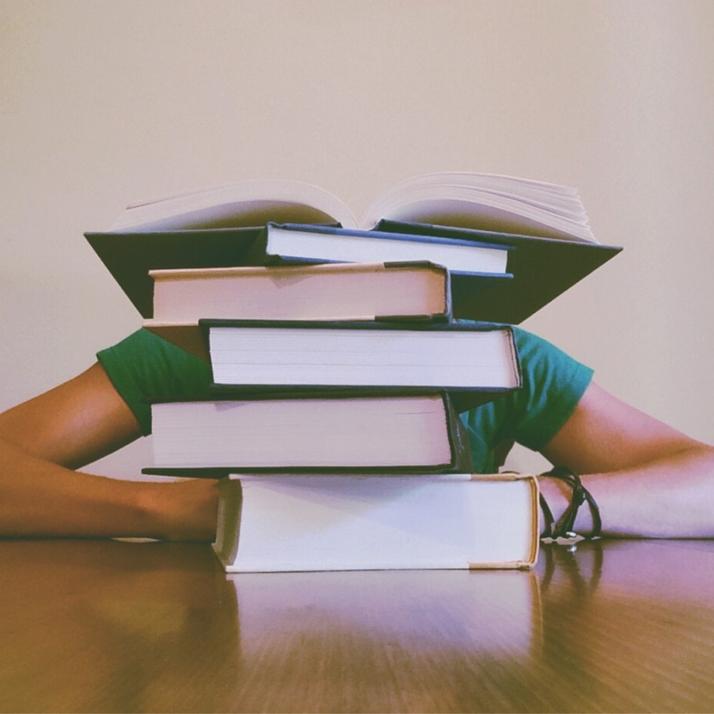 Image of a person with their head down behind a stack of books.