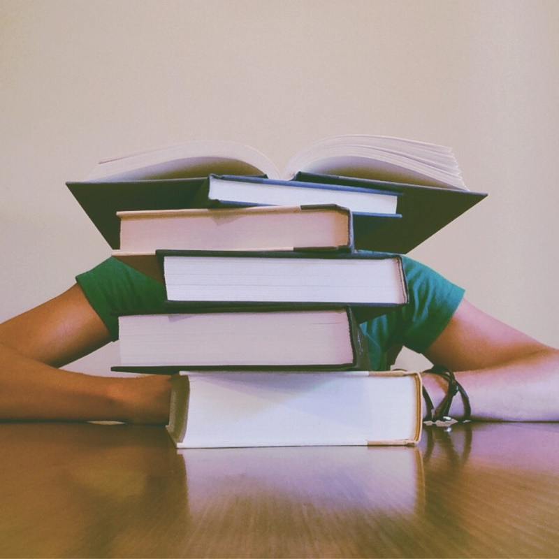 A stack of books on a desk with a figure sitting behind them.