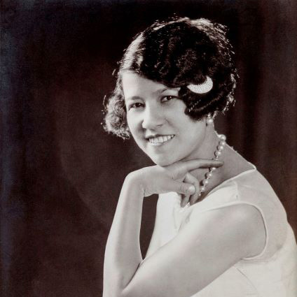 A black and white portrait of a women with her elbow resting on her knee.