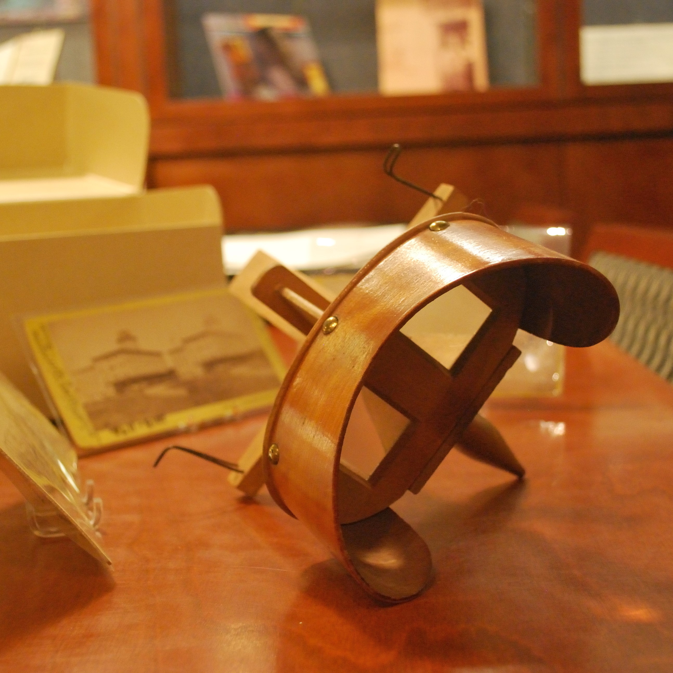 A stereoscope sits on a table with blurred photographs and file folder behind it.