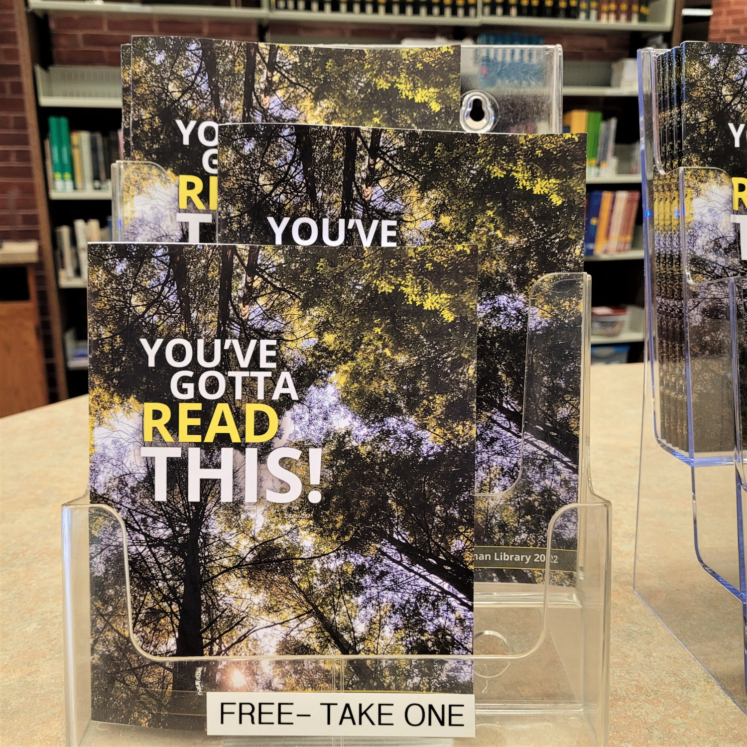 A stand of brightly colored booklets with trees on them and the words You've Gotta Read This on the cover. A white label with black text states the words Free - Take One.