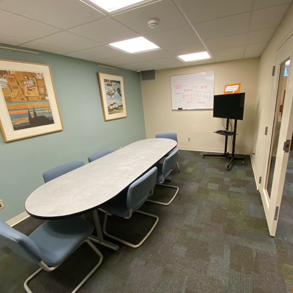 A small room with a table and six chairs. The room has a whiteboard mounted on one wall, and a TV cart for sharing from a laptop.