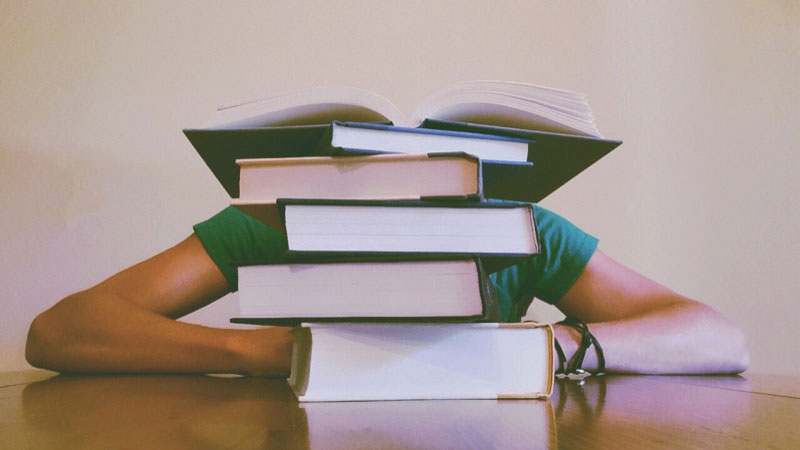 Person with their head on a desk behind a stack of books