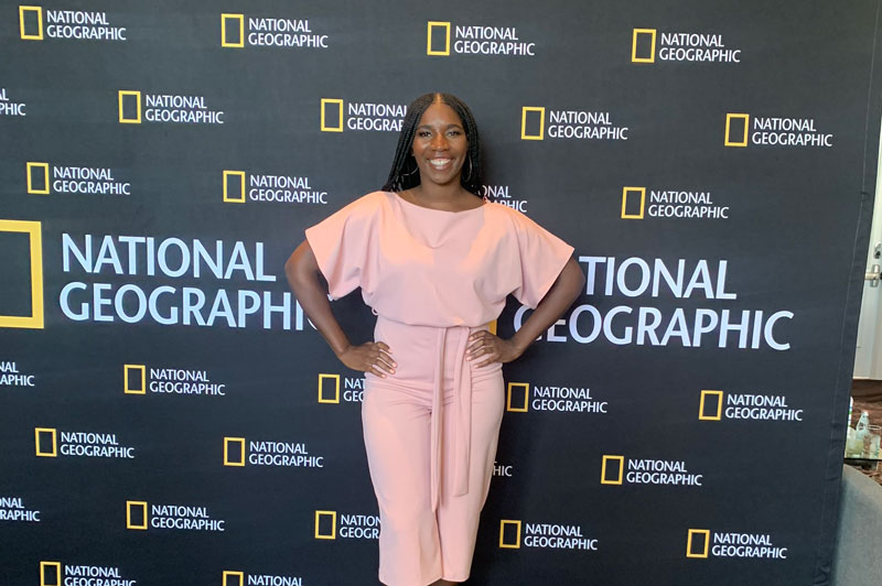 Monae Evans posing in front of wall with the National Geographic logo