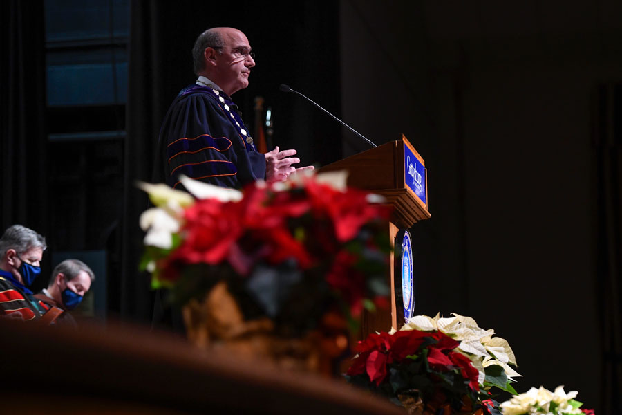 Bob Iuliano standing at a podium with flowers in the foreground