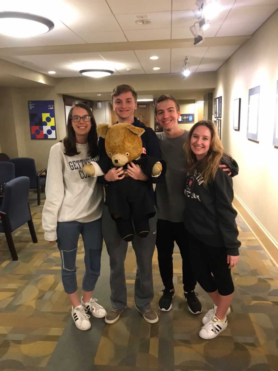 Four students standing together, one holding a large stuffed bear