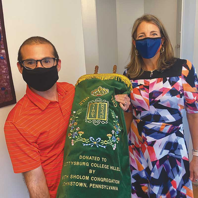 Man carrying a green Torah scroll with a mask on